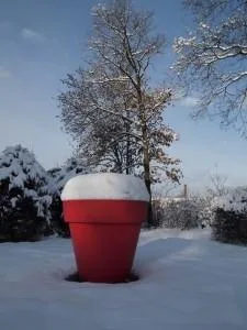 Grand pot de fleurs rouge recouvert de neige dans un jardin