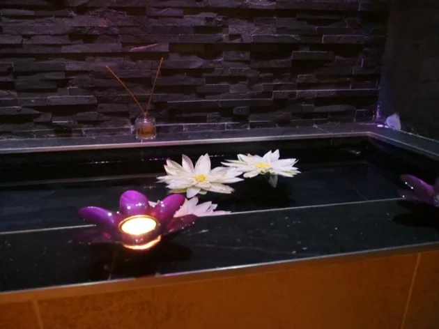Fleurs et bougie flottant dans un bassin noir au spa