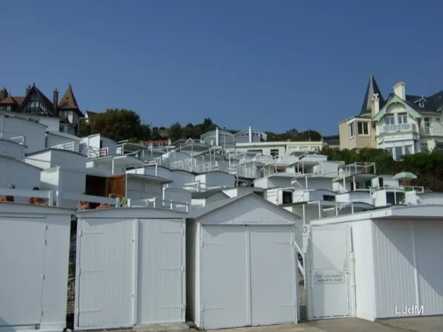 Des rangées de cabines de plage blanches sous des villas en bord de mer
