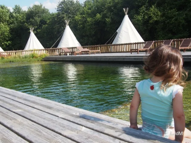 Famille vue de dos au bord d'un lac et de tentes de glamping à Echologia
