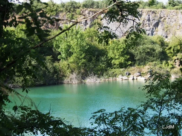 Lac de carrière verdoyant encadré d'arbres et de falaises rocheuses