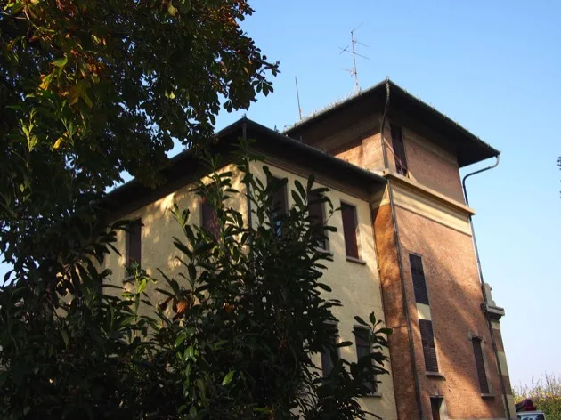 Bâtiment historique en partie caché derrière un arbre feuillu à Modène