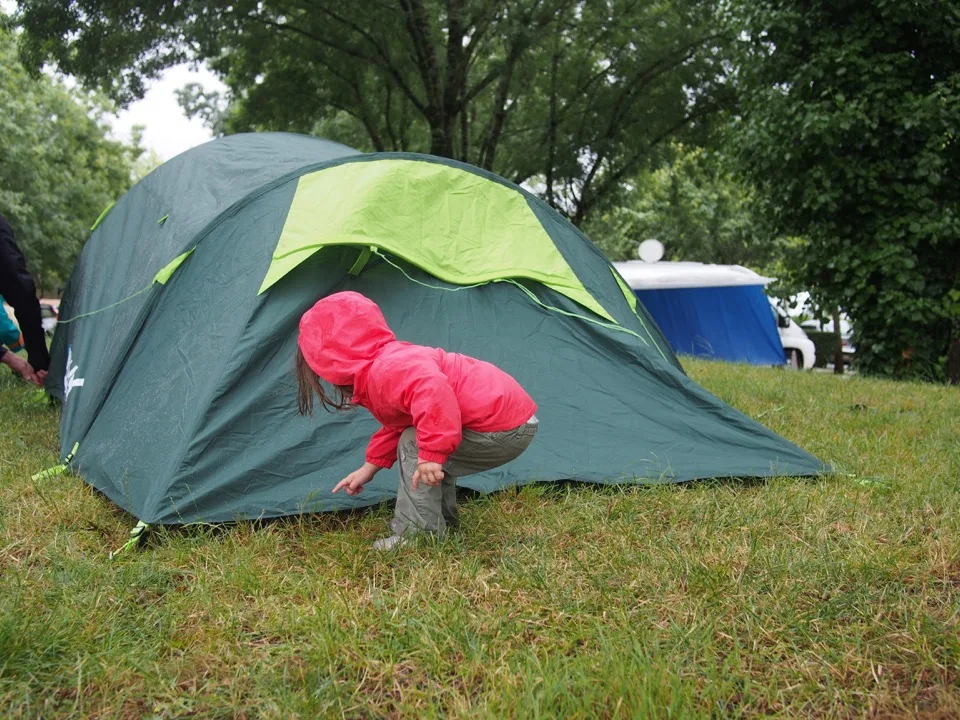 Famille installant une tente verte dans un camping boisé