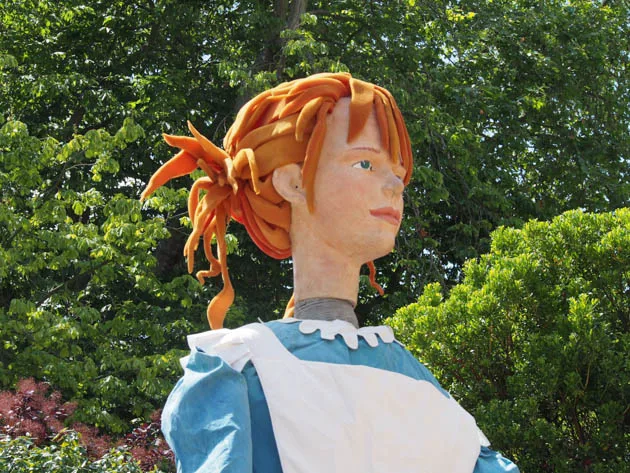 Figurine géante d'Alice vêtue d'une robe bleue sous les arbres