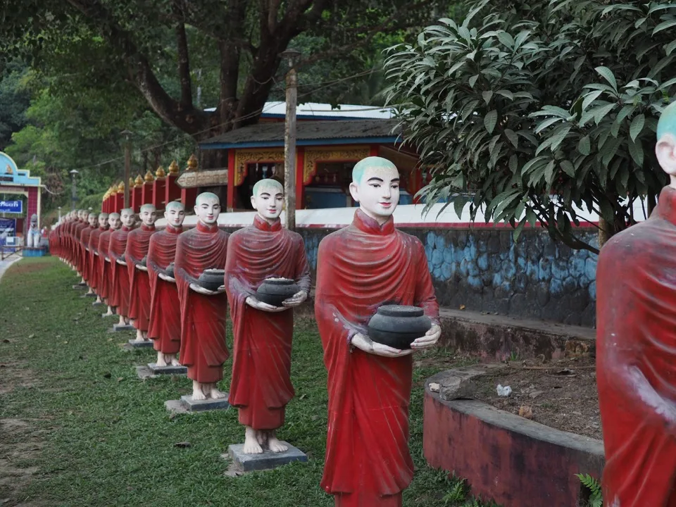 Reihe rot gekleideter Mönchsstatuen unter Bäumen
