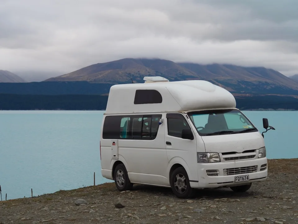 Camping-car blanc garé au bord d'un lac de montagne turquoise