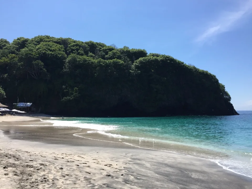 Heller Sandstrand an einer bewaldeten Landzunge auf Bali