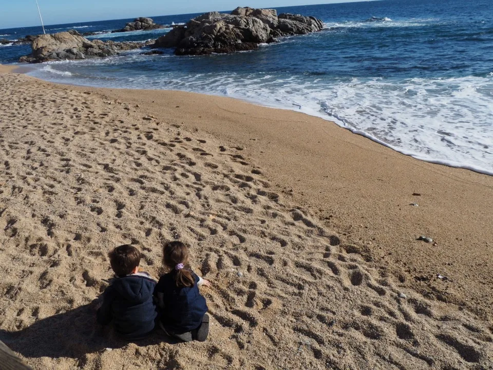 Famille de dos assise sur la plage de Calella de Palafrugell