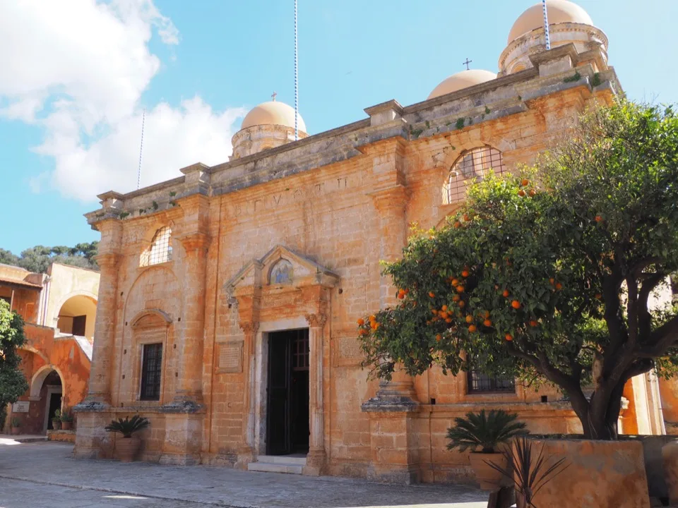 Façade of a stone Cretan monastery surrounded by orange trees